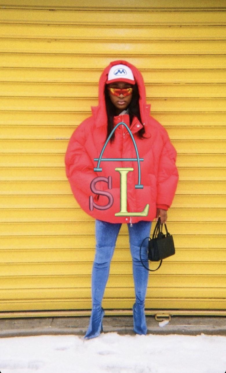 Brand shoot in a red puffer jacket against a yellow shutter, with the ASL monogram stitched on the jacket